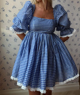 Blue and white checkered dress with puffed sleeves and lace trim against a floral wallpaper background.